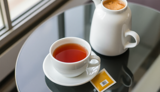White cup of tea with a saucer and a white jug on a glass table featuring Amazon Tea Coffee Premix sachet